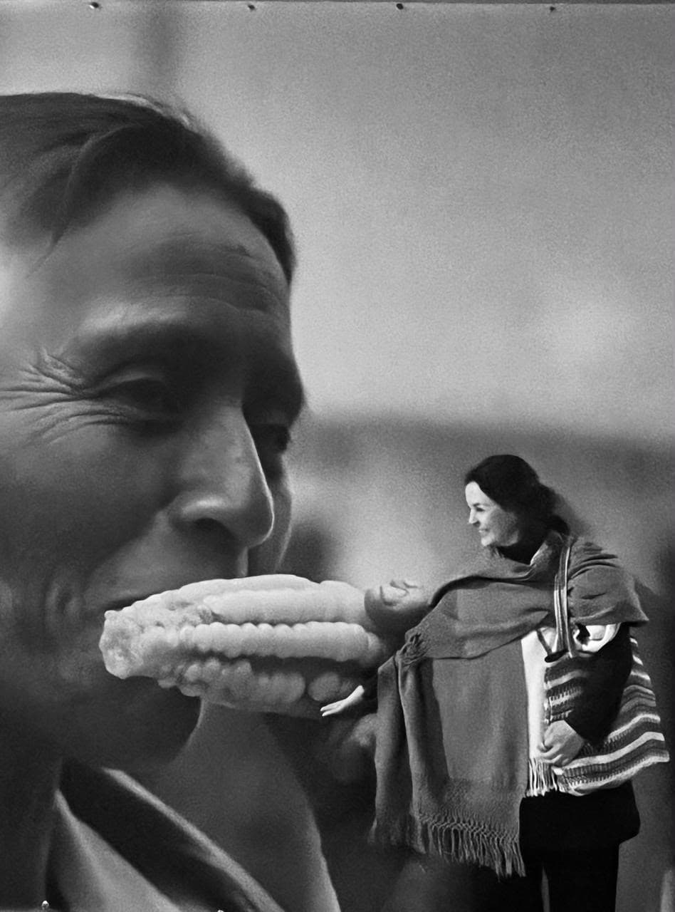 Genoveva, de pie frente a un fotomural en blanco y negro de una mujer mordiendo un elote